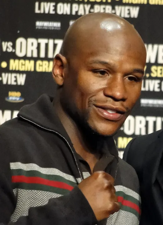 Floyd Mayweather Jr. raising a fist at a press conference backdrop