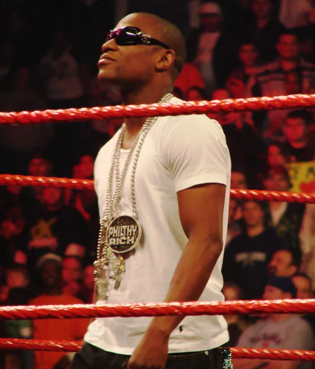 Floyd Mayweather Jr. standing in a boxing ring wearing sunglasses and chains